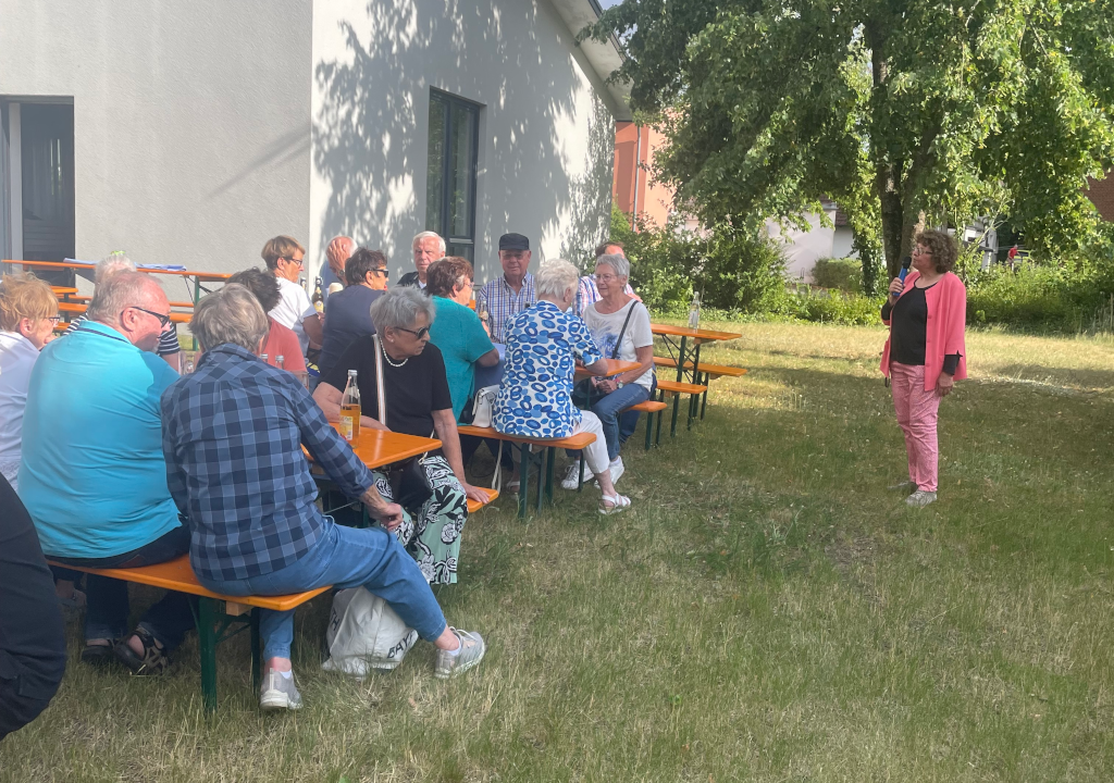 Die Tafel-Vorsitzende Ingrid Heinritzi-Martin bei der Begrüßung vor feiernden Tafelhelfern auf Bierbänken auf Bierbänken